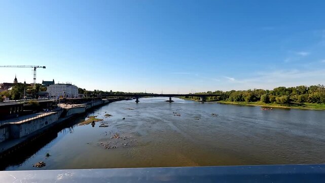 Camera movement shows the river Vistula from a bridge at the city of Warsaw. Blue clear sky at the horizon, small boats in the river.