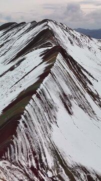 Aerial drone view of Rainbow Mountain Vinicunca in the Peruvian Andes, with multicolored peaks partly covered in snow. Located in the Cusco region, Peru.	