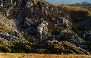 Obraz premium Female traveler walking on green hill slope, admiring epic landscape view. Small person big nature concept