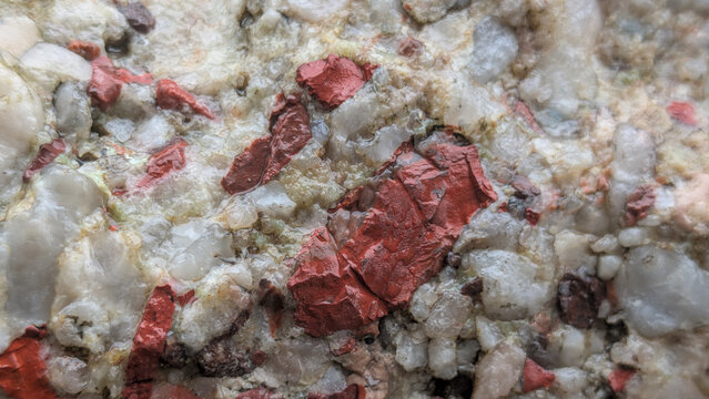 Close-up view of a textured rock with red mineral inclusions and quartz crystals, background, texture