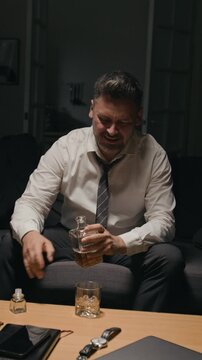 Vertical video of middle aged Caucasian man pouring whiskey from decanter, drinking alone. Suitable for campaigns addressing stress, substance abuse and mental health