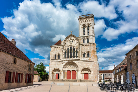 Vezelay Abbey, a UNESCO World Heritage site, displaying Romanesque architecture with its ornate facade, central tower, and red doors under a dramatic cloudy sky