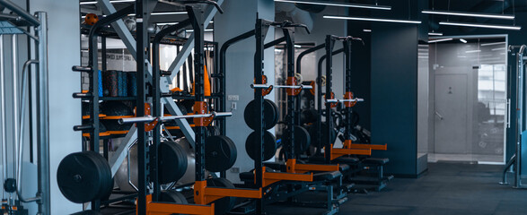Fototapeta premium Focused Gym Equipment For Weight Training And Fitness, Barbell And Weight Plates Available In Stylish Modern Gym Setting. Ideal For Weight Loss Concept, Training And Exercise Enthusiasts.