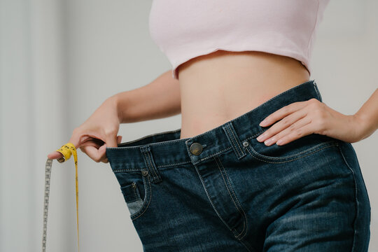 Weight loss success concept, slim woman shows oversized jeans and measuring tape after losing weight at home, weight loss, diet, fitness, healthy lifestyle, body transformation