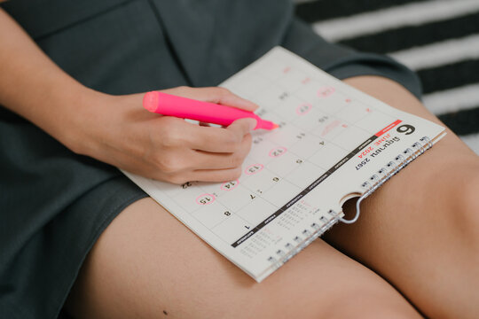 Menstrual cycle tracking concept, woman marks period dates on calendar to monitor menstruation, reproductive health, fertility, ovulation, period, cycle tracking