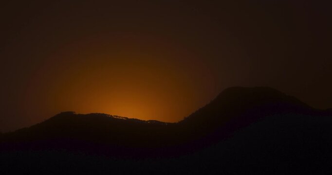 Timelapse of the sun rising behind the mountain silhouette