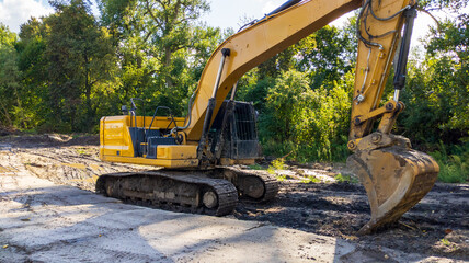 Yellow Excavator Digging Dirt on Construction Site with Big Bucket Machinery and Green Trees Background © yaviki