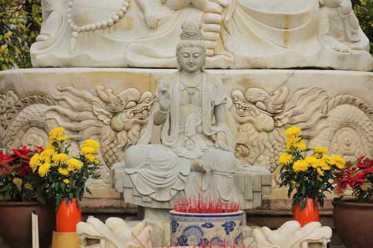 Stone Guanyin statue at Buddhist temple altar with yellow chrysanthemum flowers and smoking incense burner in Da Nang, Vietnam