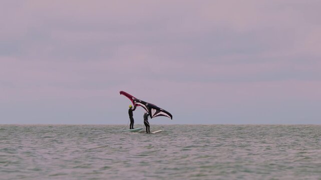 An athlete standing on the board holds on to the wing, in which the wind creates thrust in slow motion. Wingfoil board where a surfer glides through the water on a hydrofoil board..