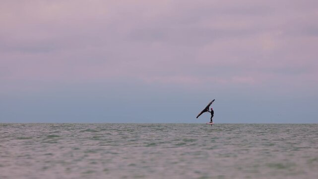 An athlete standing on the board holds on to the wing, in which the wind creates thrust in slow motion. Wingfoil board where a surfer glides through the water on a hydrofoil board..