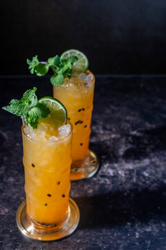 Passionfruit cocktail with mint and lime garnish on a dark surface 