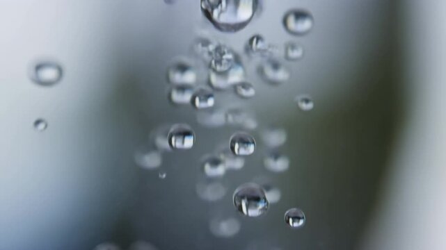 Slow motion close up of water droplets falling on glass pane with blurred background