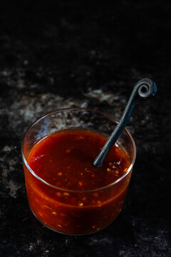 Chili paste in a container with a spoon on a dark surface 