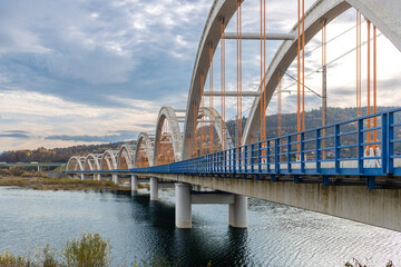 Dramatic perspective along the concrete railway arch bridge near Zembrzyce and Jezioro Mucharskie. Repeating arches, orange vertical hangers, blue railing and reservoir water create strong commercial  © Volha