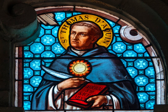 Saint Thomas Aquinas appears on a stained glass window holding a quill and a book.