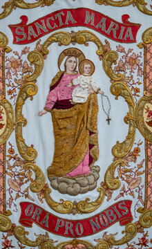 An embroidered religious banner depicts Virgin Mary holding infant Jesus surrounded by ornate golden thread floral patterns.