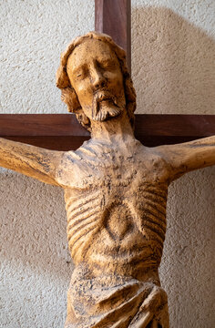 A hand carved wooden statue depicts Jesus Christ affixed to a dark wooden cross indoors.