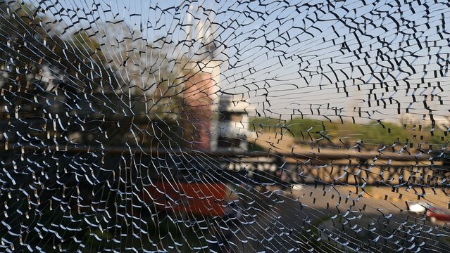 Dramatic close up of shattered glass with extensive radial cracks over a blurred urban street scene, creating a powerful visual metaphor for damage, vulnerability, impact and disruption
