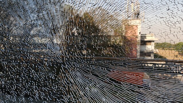 Dramatic close up of shattered glass with extensive radial cracks over a blurred urban street scene, creating a powerful visual metaphor for damage, vulnerability, impact and disruption