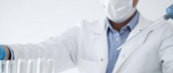 Scientist wearing protective gloves. Mask. And glasses carefully transferring clear liquid between...