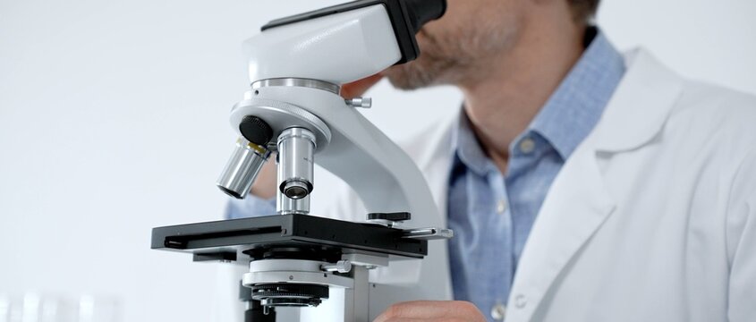 Scientist looking through a microscope in a bright laboratory, performing medical research and scientific discovery, exploring microbiology and biochemistry for new solutions
