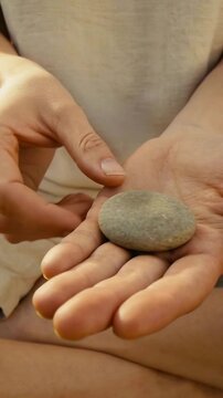 Vertical video: Placing pebble on palm, man's hands rubbing it with finger on lap in tank top