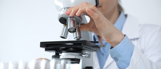 Fototapeta na wymiar Scientist wearing protective gloves and a face mask performing scientific research using a microscope in a bright laboratory