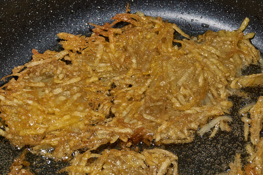 Large grated potato fritter cooking in a frying pan. Hot oil bubbles around the potato pancake as a golden crispy crust forms during frying. Homemade potato pancake made from coarsely grated potatoes.