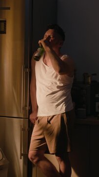 Vertical shot of middle aged Caucasian man drinking beer bottle with troubled expression. Footage ideal for mental health awareness and substance abuse rehabilitation campaigns