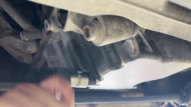 A person is working on a car engine. The engine is black and the person is using a wrench to loosen a bolt
