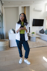 Obraz premium Woman standing in center of modern living room holding smartphone and wearing eyeglasses