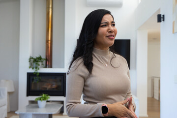Obraz premium Woman standing right in living room wearing beige sweater with clasped hands showing smartwatch