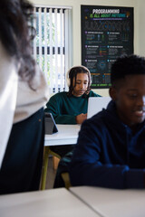 Diverse classmates including youth male with braided hair working on silver laptop in classroom © WavebreakMediaMicro