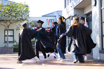 Group of graduates celebrating in campus courtyard, wearing gowns and caps, holding diploma scrolls © WavebreakMediaMicro