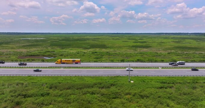 Long straight expressway in Florida with fast moving vehicles flanked by open marshland and clear skies.