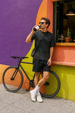 Urban cyclist drinking from blank cold brew bottle by colorful cafe