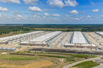 Obraz premium Aerial view of a large data center under construction with expansive industrial buildings, white roofs, parking lots, and surrounding green fields in United States