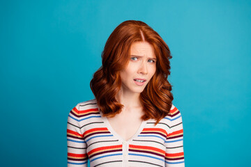 Fototapeta premium Confused redhead woman looking skeptical and doubtful in a casual striped sweater studio portrait against a bright blue background expressing puzzlement