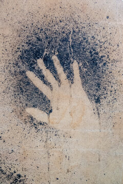 A negative hand stencil is painted using dark pigment on a stone.