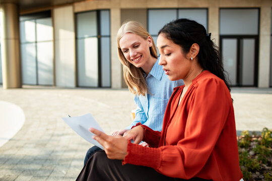 Two colleagues discussing a document outside a modern office