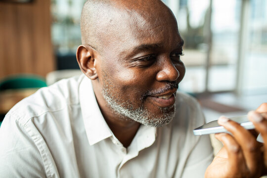 Smiling mature man using smartphone voice assistant indoors