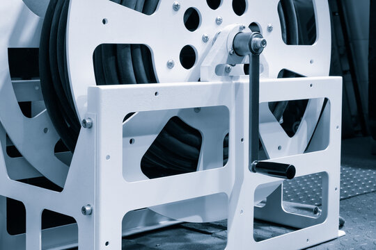 White cable reel sits on metal base. Black cables are wound around its center. Electrical network repair machine