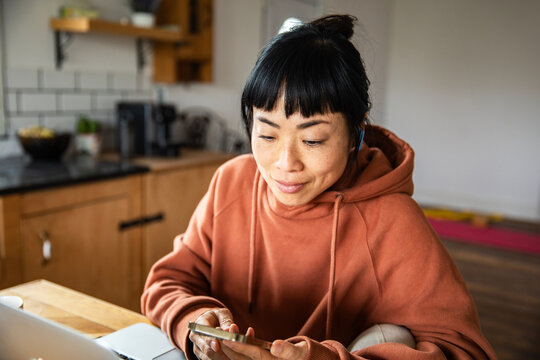 Smiling woman using smartphone at home kitchen table