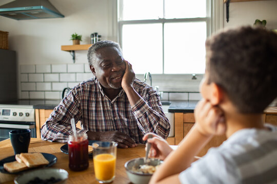 Senior man and boy talking at kitchen breakfast table