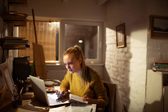 Young woman studying on laptop in cozy home office at night