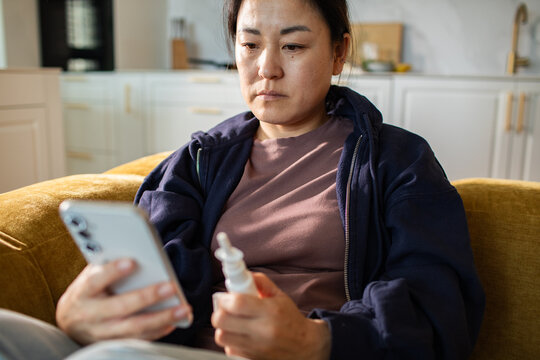 Woman checking phone while holding nasal spray at home