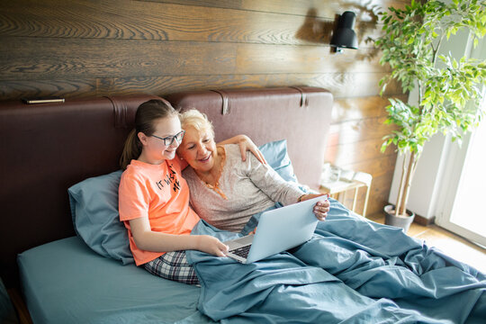 Grandmother and granddaughter using laptop in cozy bedroom