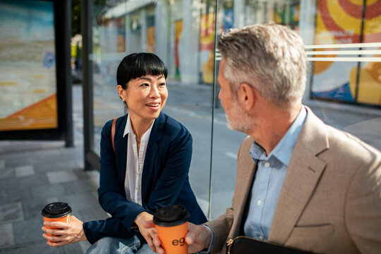 Business colleagues chatting over coffee at urban bus stop