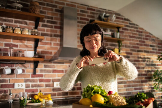 Woman photographing fresh vegetables in home kitchen
