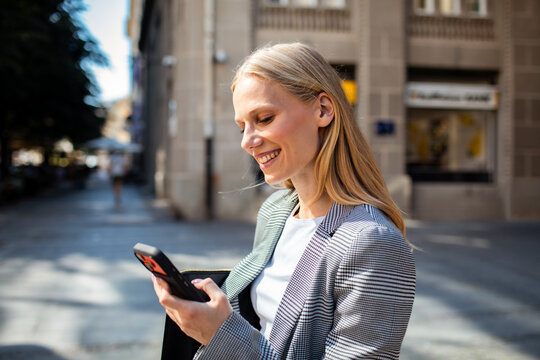 Smiling businesswoman using smartphone on city street